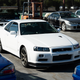a white r34-generation nissan gt-r parked in a storage lot among numerous other JDM vehicles at an export facility in japan